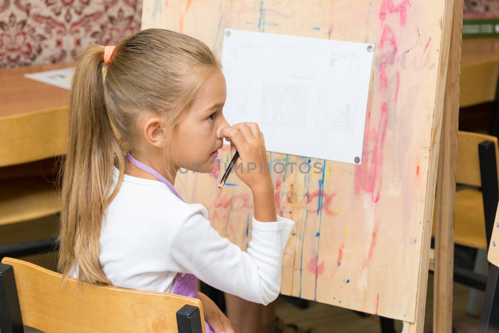 Girl scratching nose listening to the teacher carefully at drawing lesson
