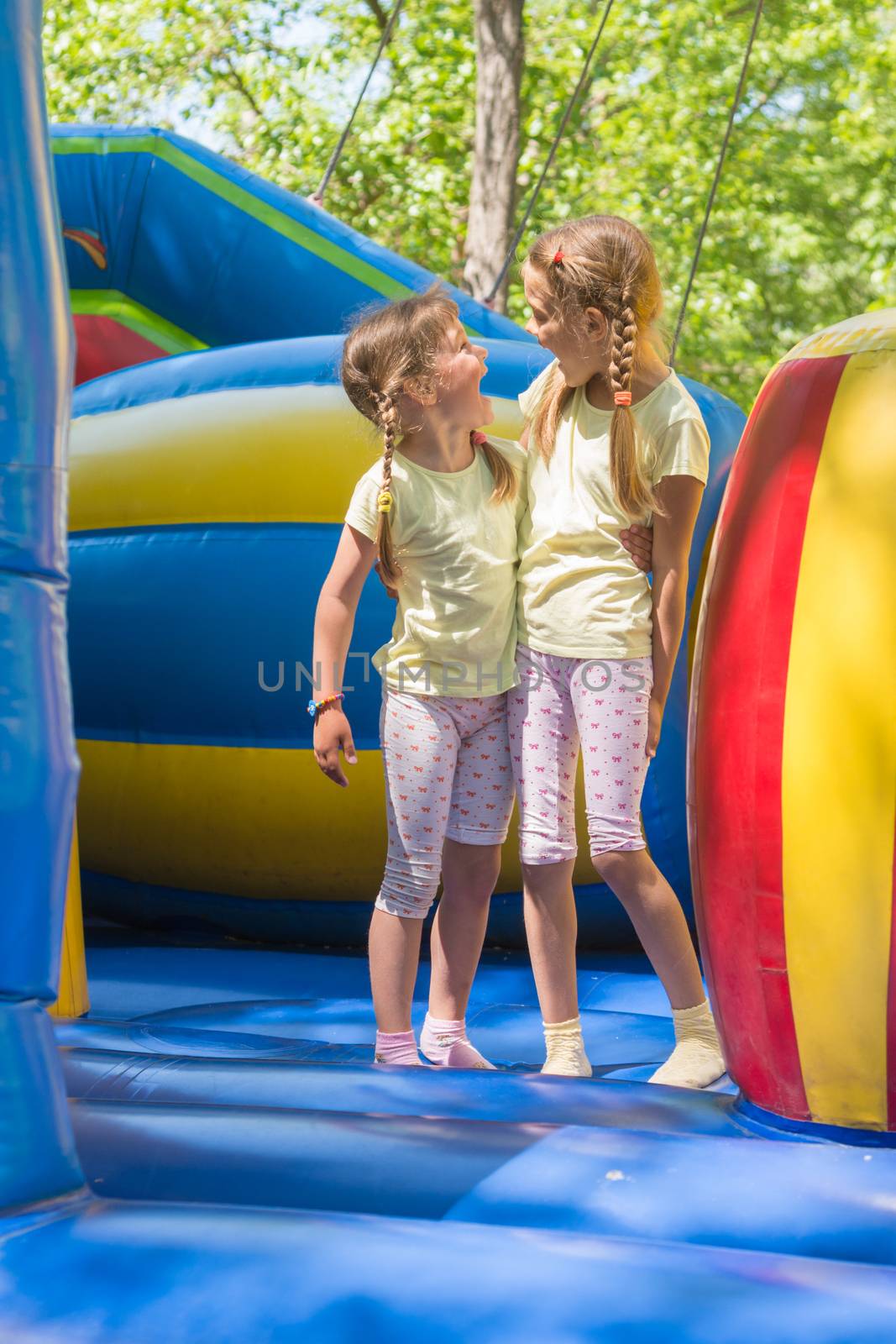 Two girls grimacing happily looking at each other by jumping on an inflatable trampoline