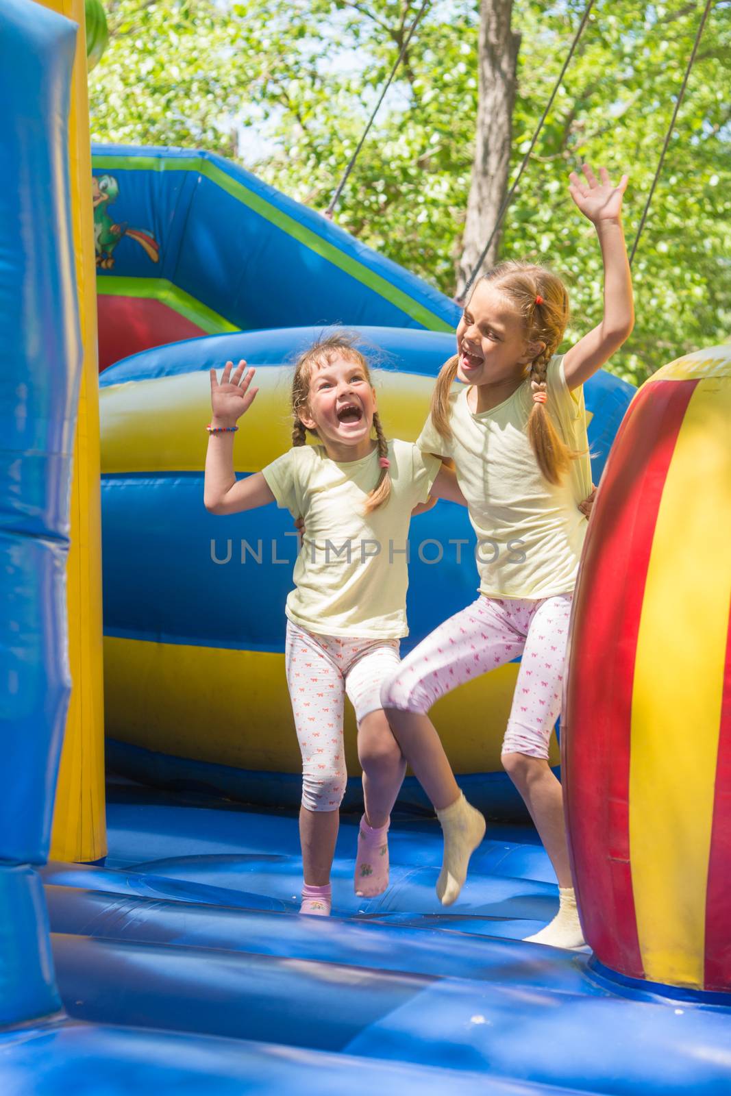 Two girls grimacing happily jumping on an inflatable trampoline by Madhourse