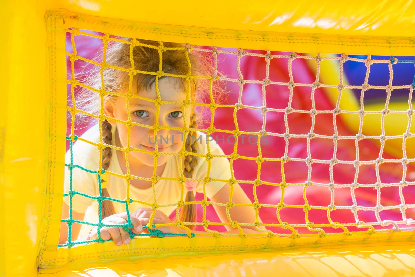 A five-year girl is looking through a mesh trampoline inflatable