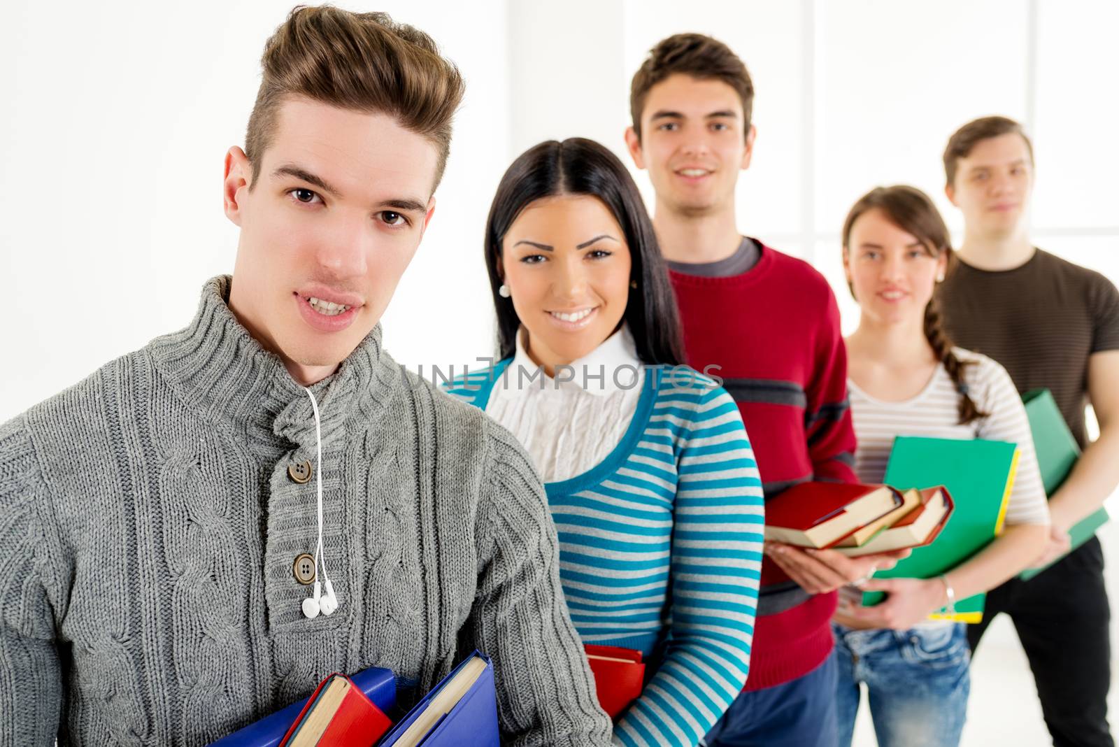 Group of happiness students with books standing in school hall and looking at camera. Selective focus.