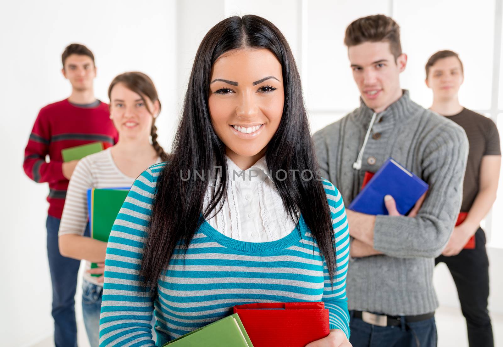 Group of smiling students with books standing in school hall and looking at camera. Selective focus.