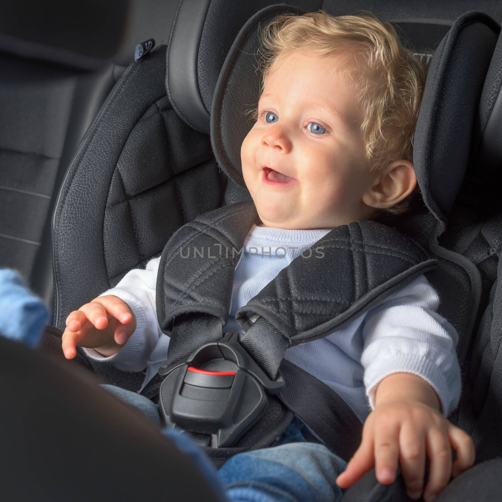 Baby boy 8 months old smiling in a safety car seat.