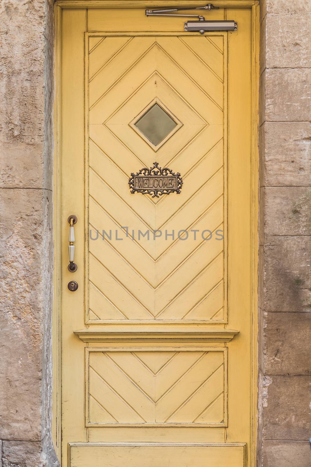 Old yellow wooden door with a small window and welcome sign at Stone House