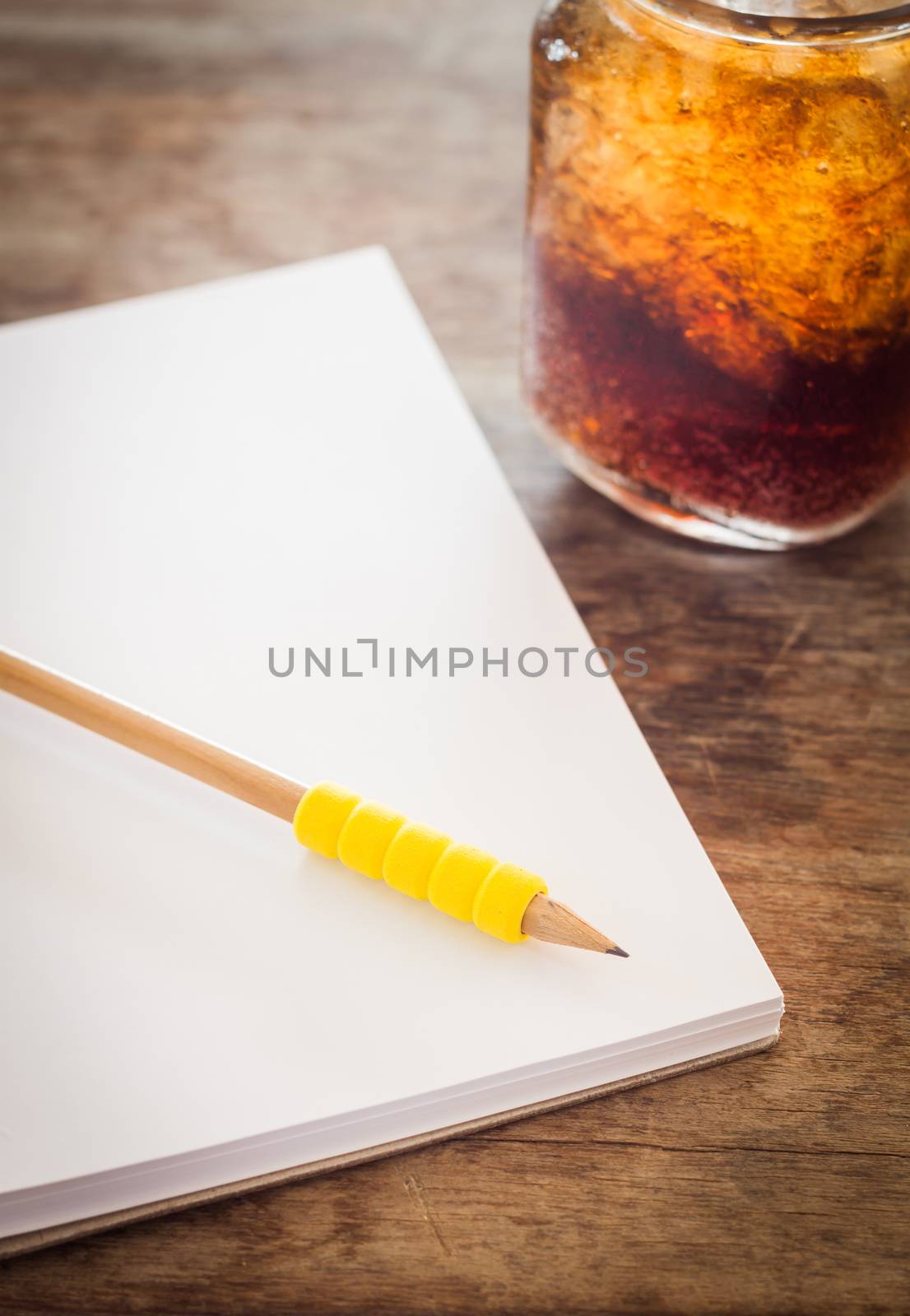 Pencil on open blank notebook with glass of iced cola, stock photo