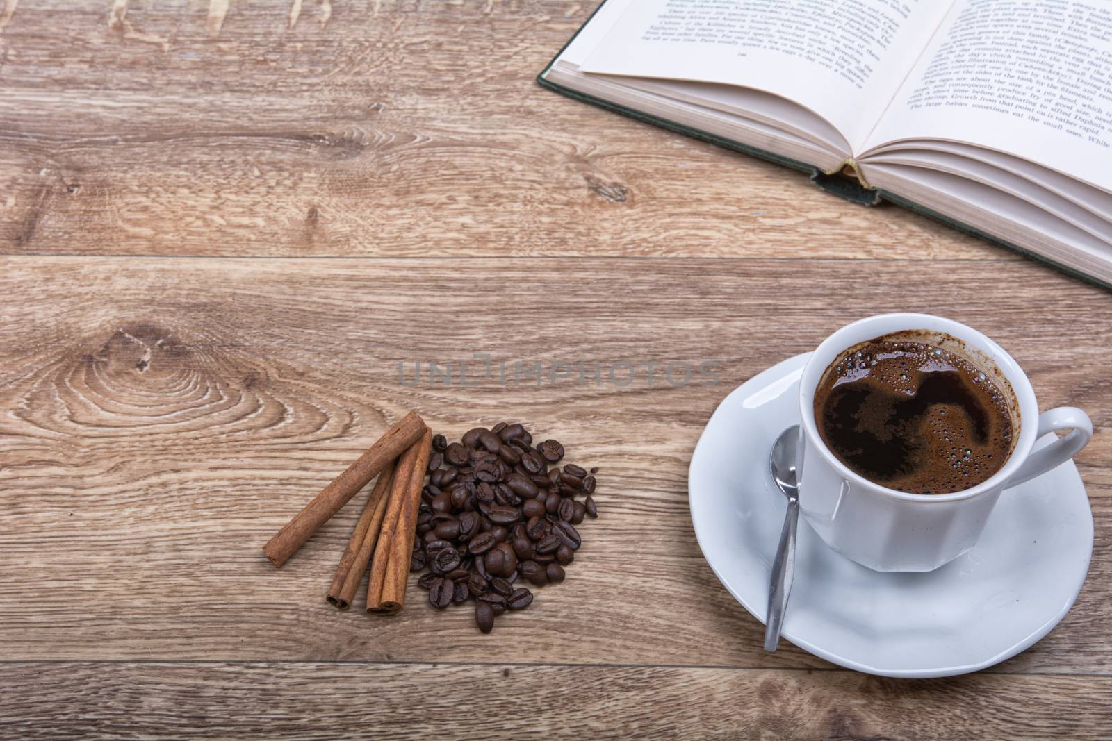 A cup of coffee and cinnamon with a book on a wooden background