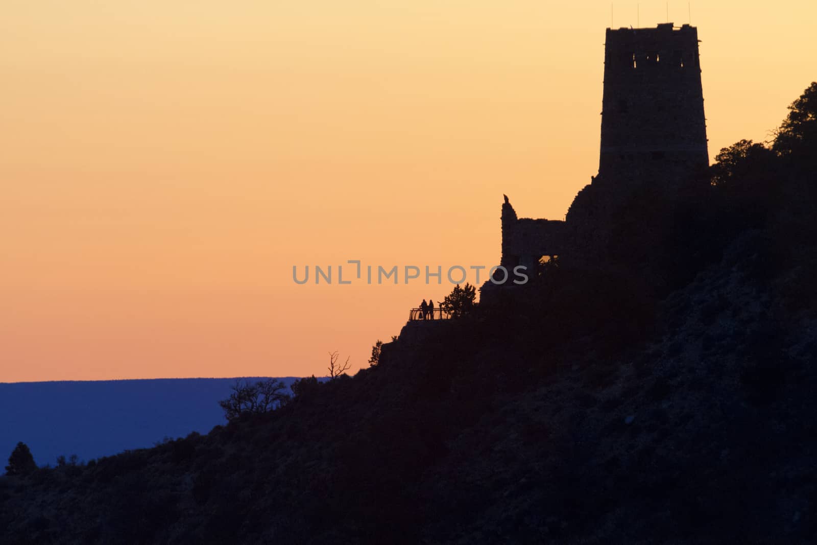 Sunrise colors the sky seen from Grand Cayon's Navajo Point along the South Rim's Desert View Scenic Drive.  Distant silhouette of couple at the Watchtower adds to scene's serenity. 