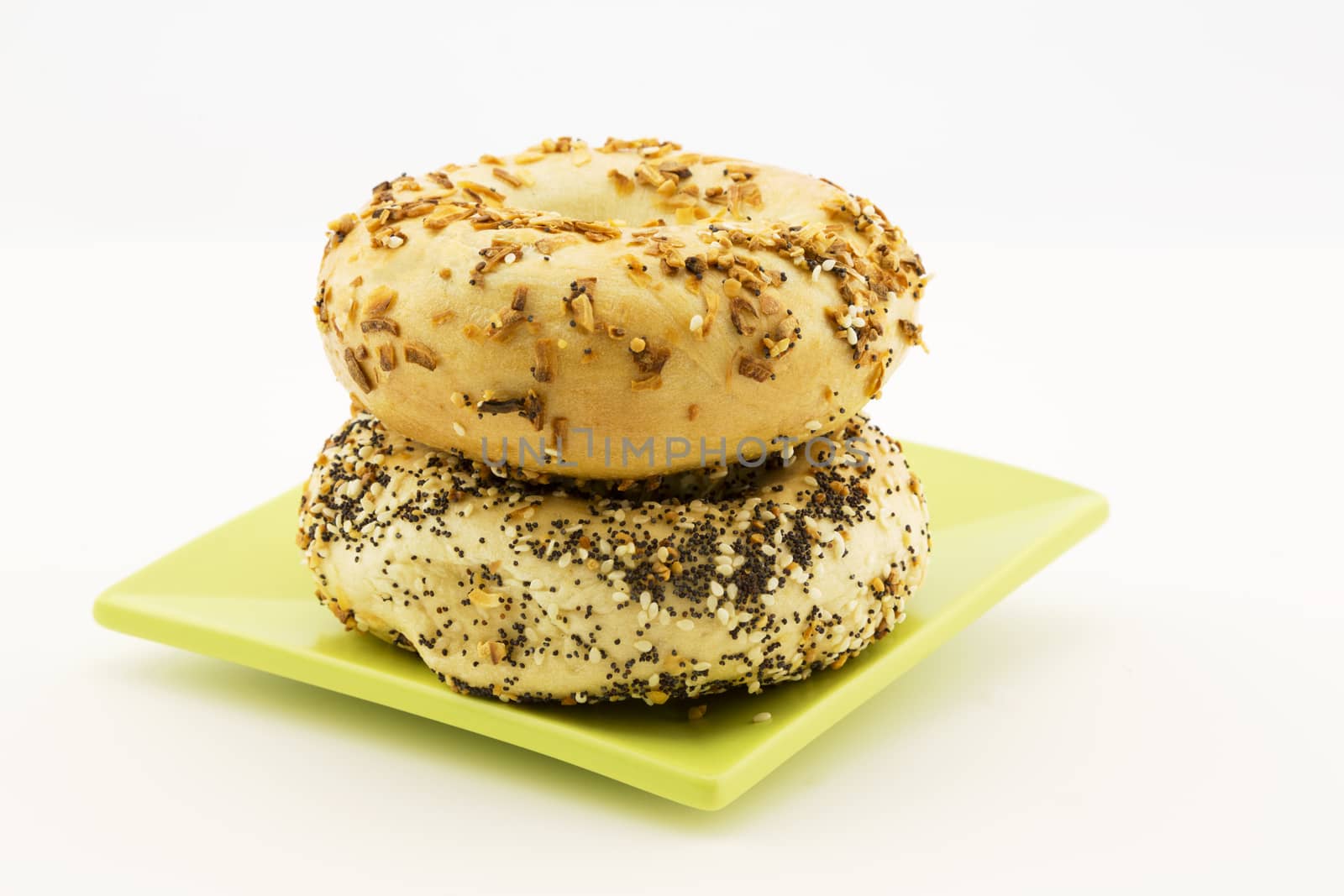 Two specialty bagels are a short stack on plate in horizontal image.  Types are Onion and Everything and make for a tasty choice.  