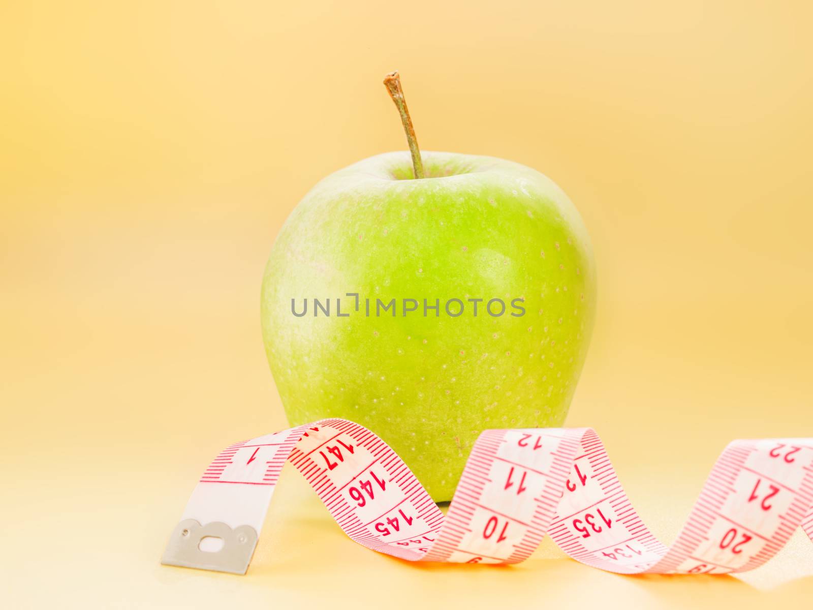 Measuring tape and delicious green apple on bright yellow background. Diet or healthy eating concept.