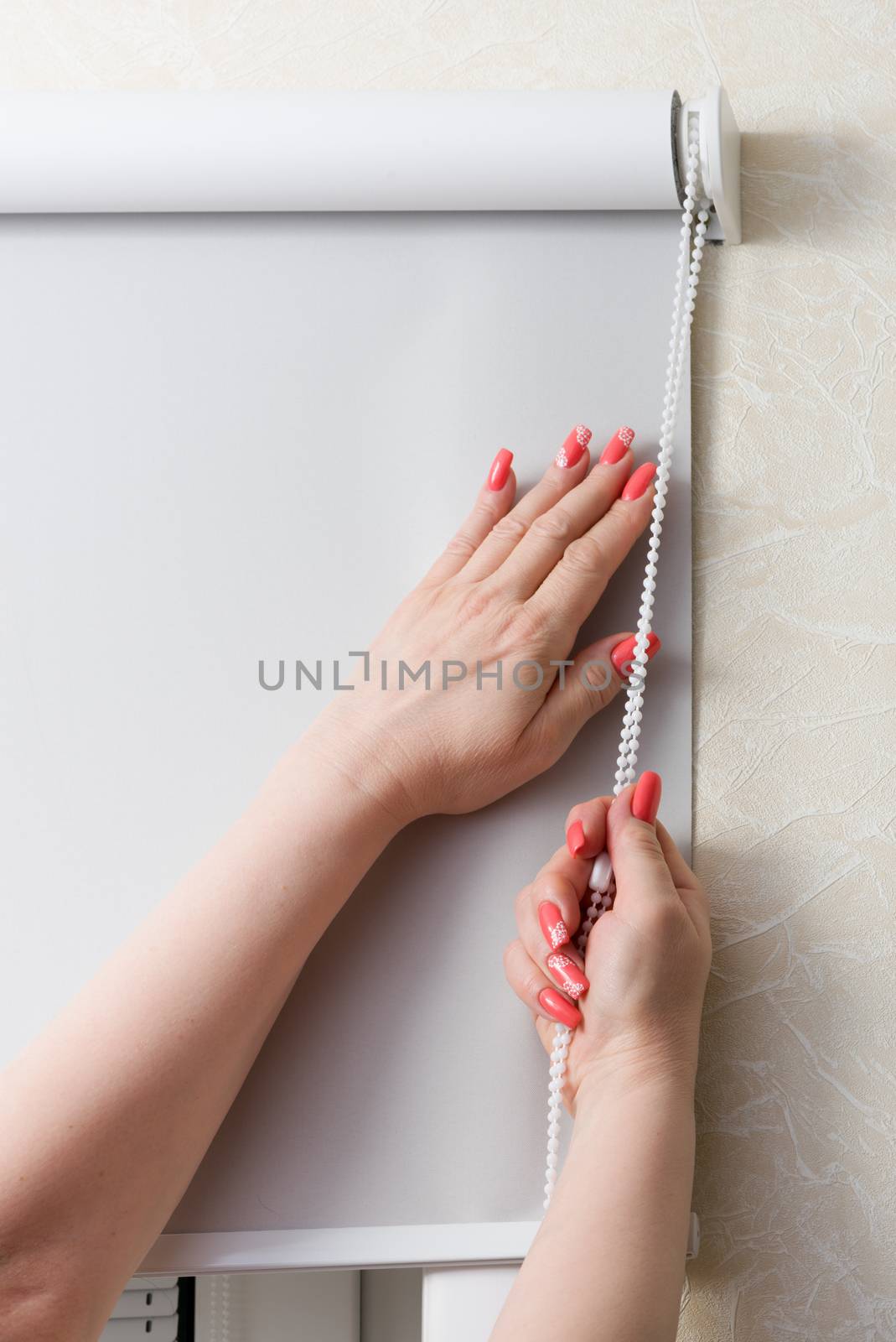 Female hands whith manicure close rolling shutters and blinds at window by fotooxotnik