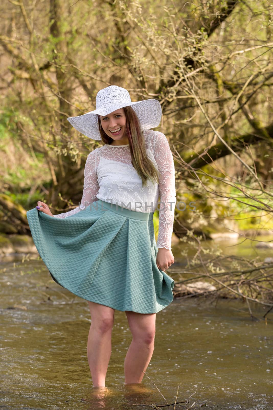 Cheerful fashionable woman in stylish hat and frock posing outdoor in creek. Happy brunette girl with long hair in warm spring day