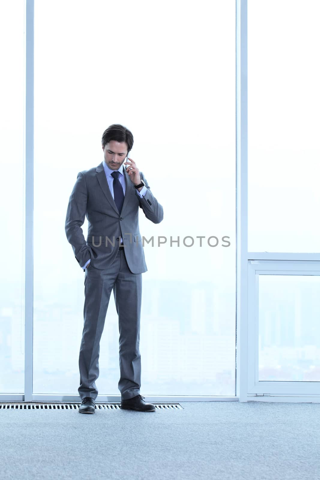 Businessman standing near window, looking at city and talking by phone