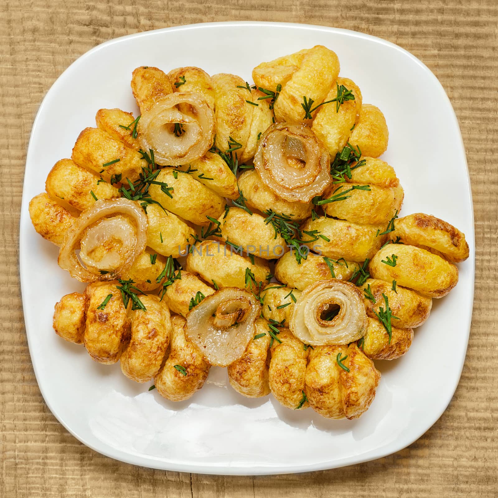 Fried potatoes cut in a spiral, on a white plate and wooden background