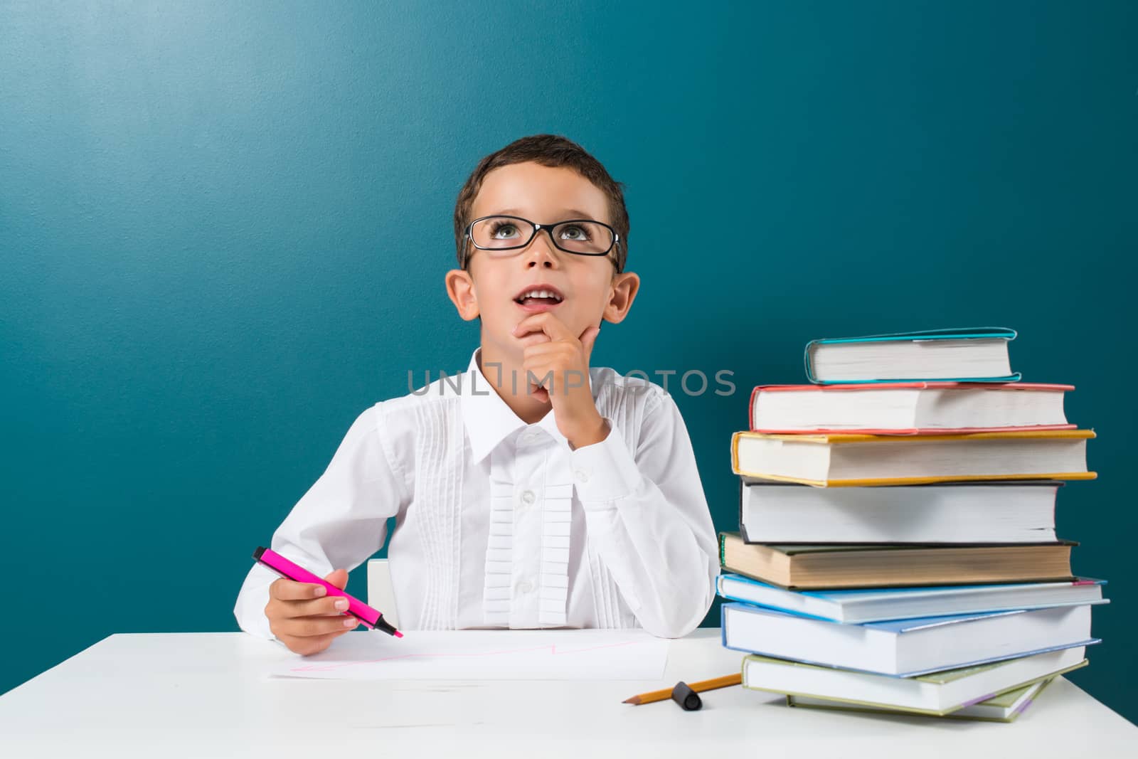 Cute little boy with books on the table, blue background