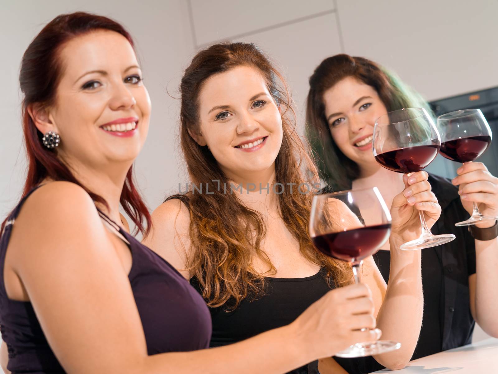 Photo of three female friends toasting with red wine at a party. Focus on middle woman.