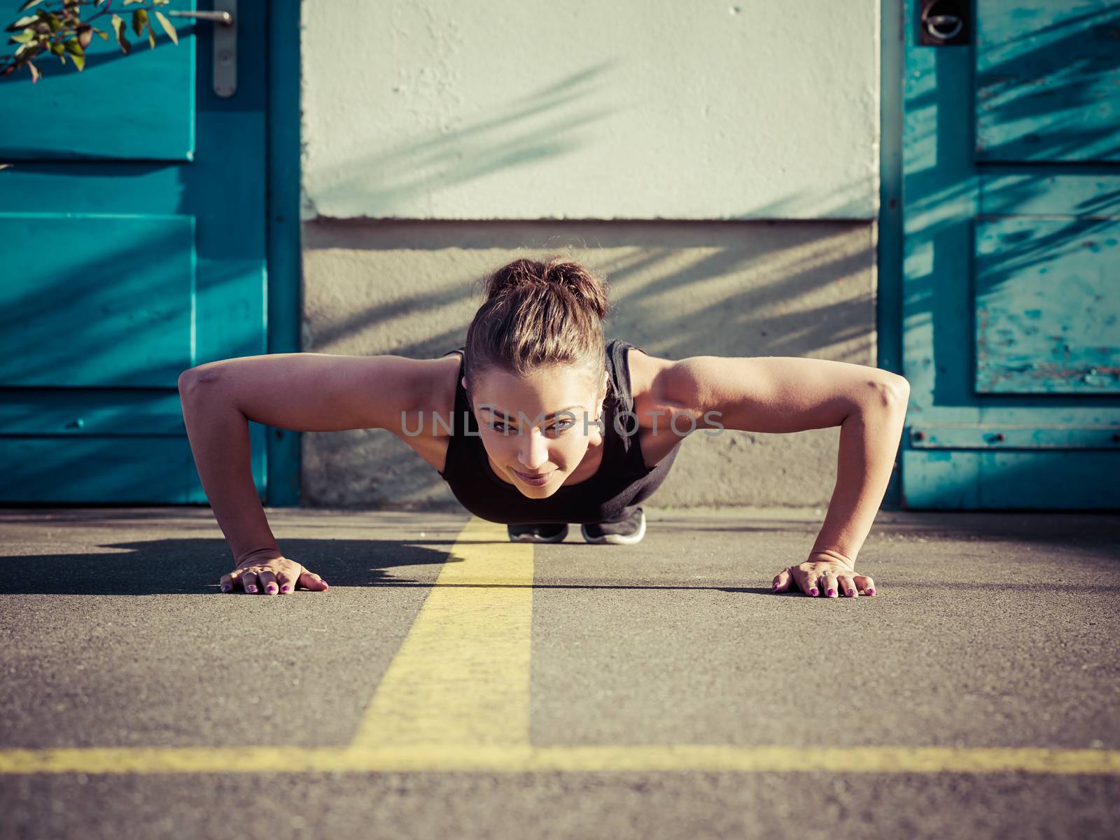 Photo of a toned young woman outside on the pavement doing pushups late in the day.
