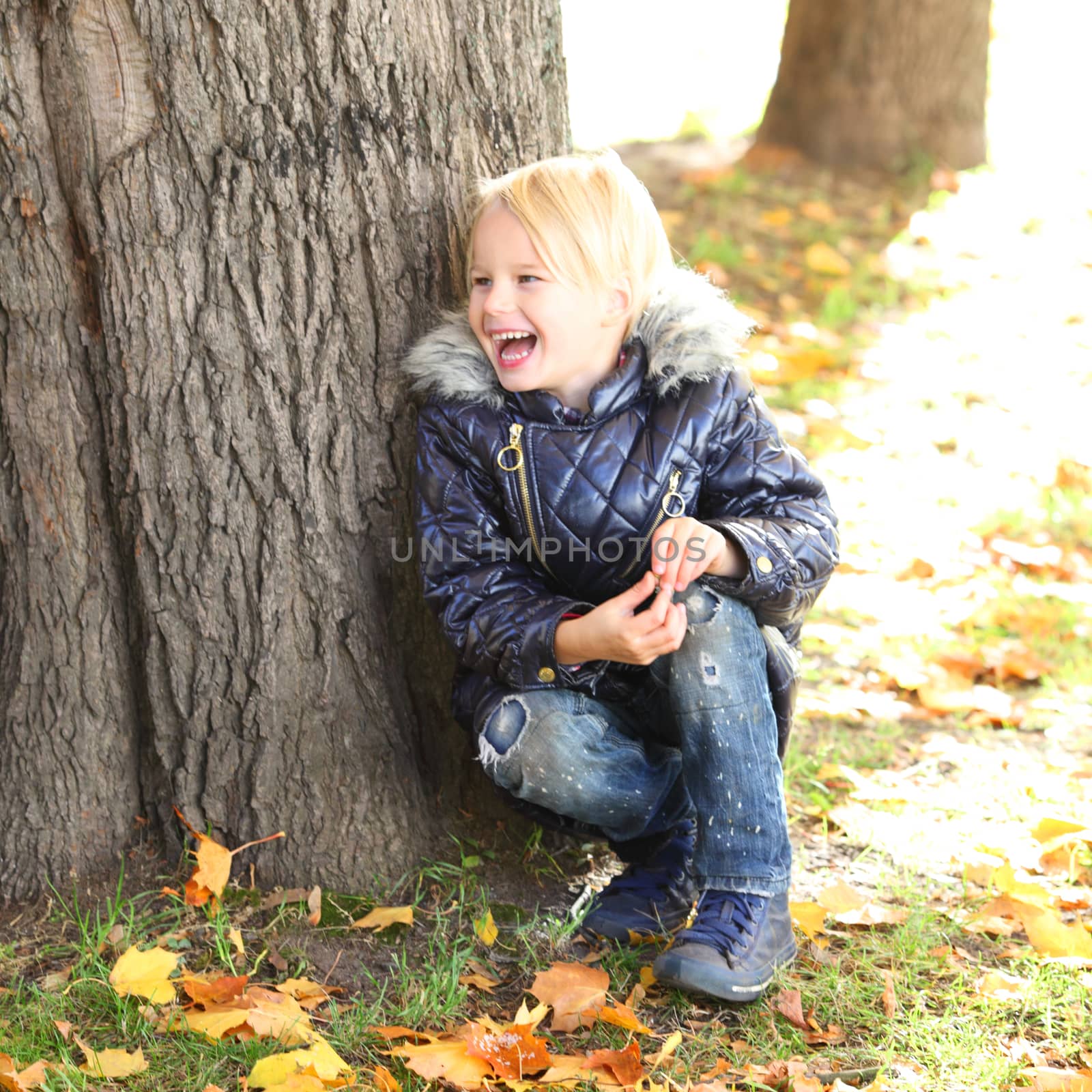 Happy child laughing sitting near tree in autumn park