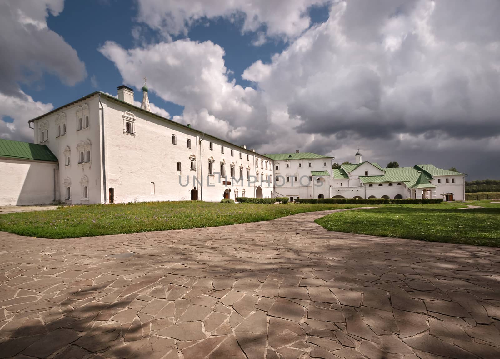 The buildings of the old monastery in Suzdal, Russia. Green grass and stone slabs in the yard.