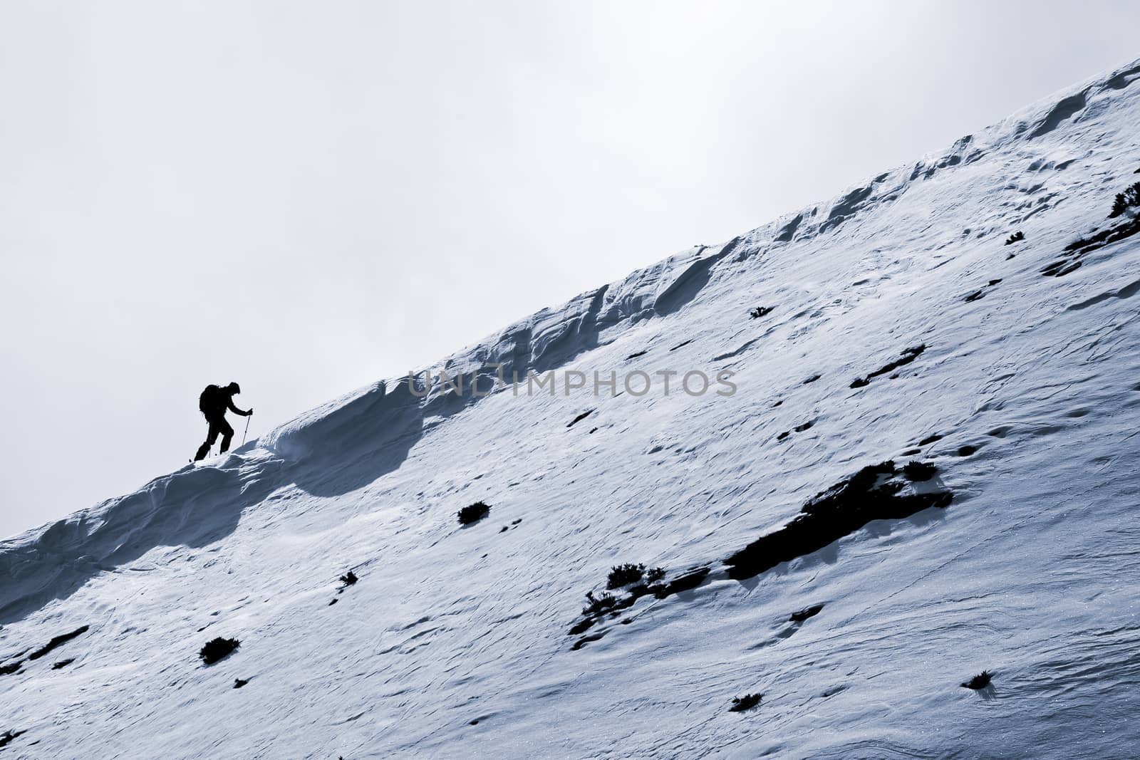 Small figure of skier, climbing a mountain