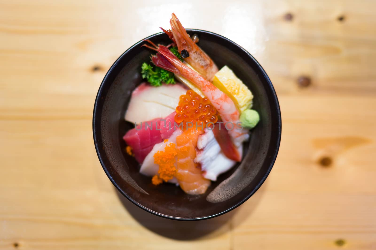 Chirashi sushi, Japanese food rice bowl with raw salmon sashimi, tuna, and other mixed seafood, top view, center aligned with copy space on wooden table, focus on salmon eggs with depth of field effect