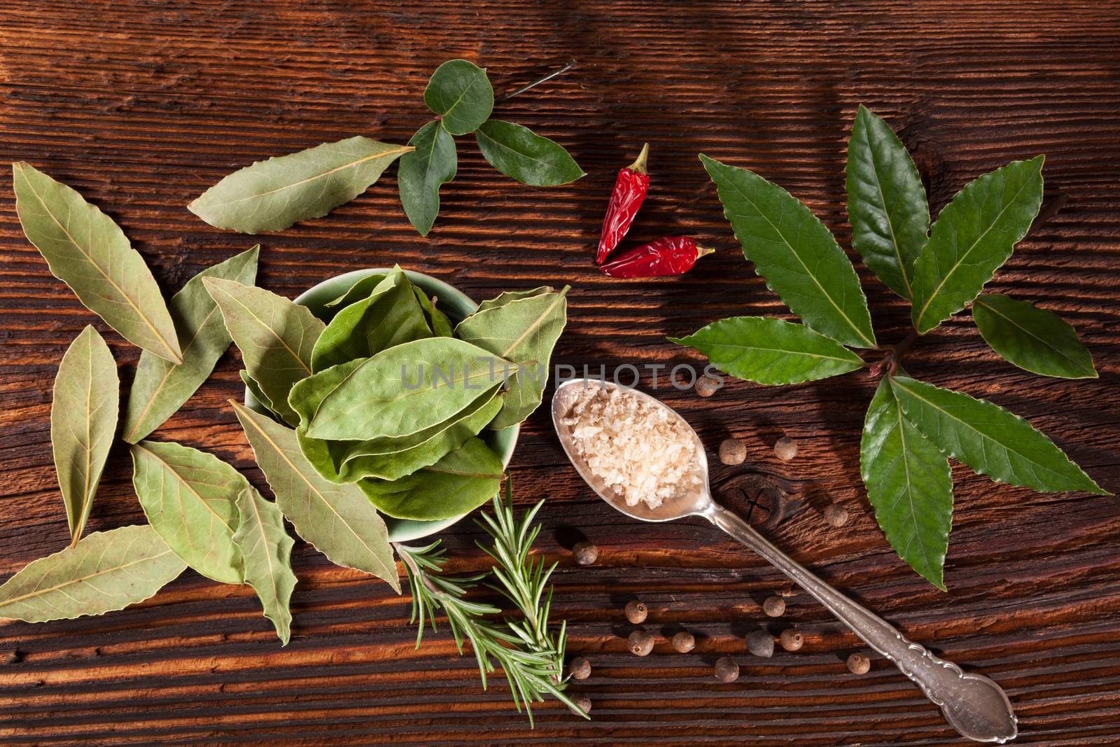 Traditional spice and condiment wooden background. Bay leaves, rosemary, chillies and black pepper on brown wooden table, top view.
