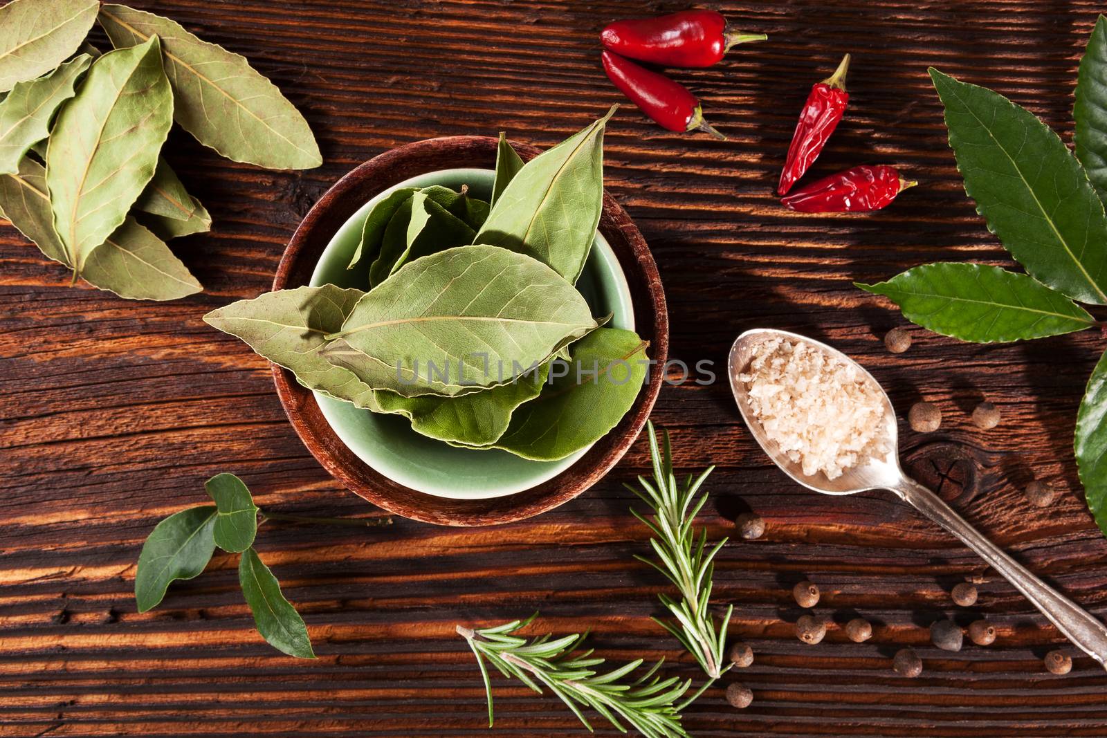 Traditional spice and condiment wooden background. Bay leaves, rosemary, chillies and black pepper on brown wooden table, top view.