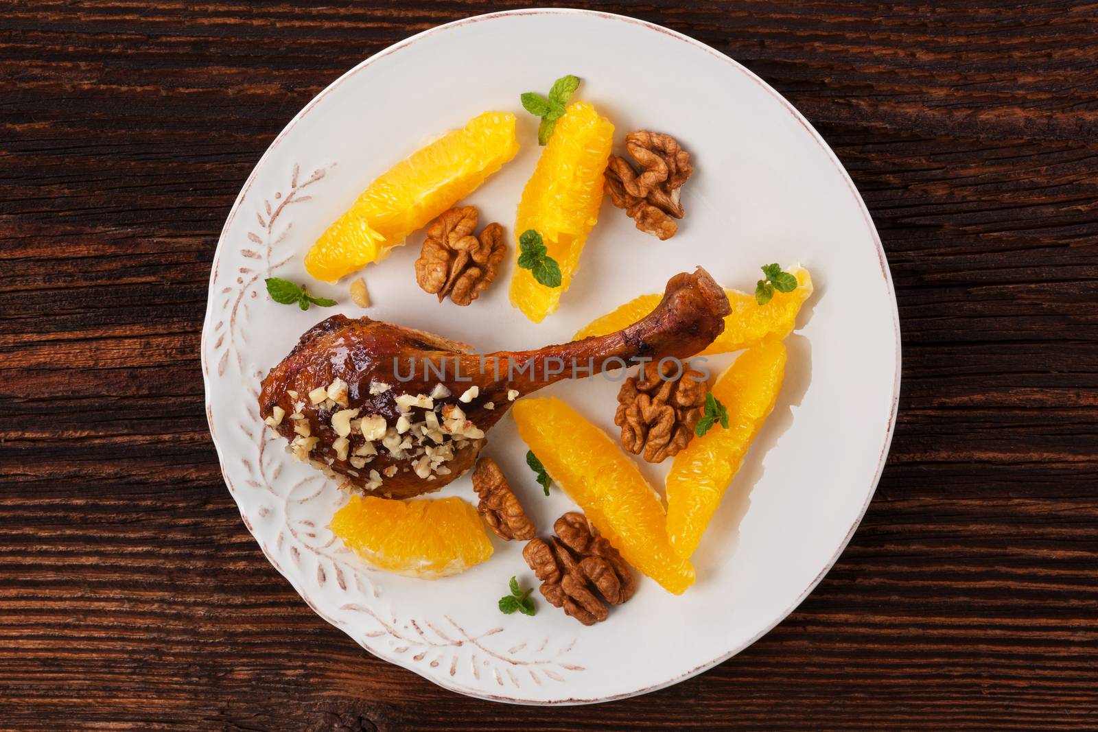Luxurious roast duck with fruit and nuts on plate on wooden background, top view. Culinary roast duck eating. 