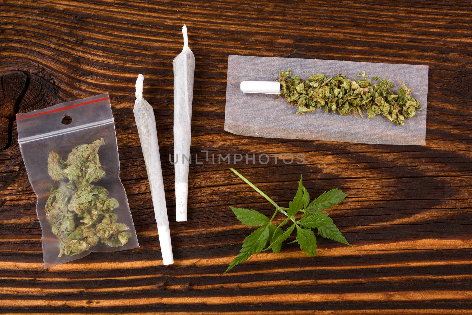 Marijuana background. Cannabis joint, bud in plastic bag and hemp leaves on wooden table. Addictive drug or alternative medicine. 