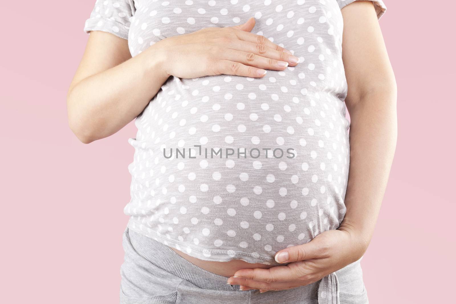 Pregnant beautiful woman touching big belly isolated on pink background. Pregnancy and motherhood. 