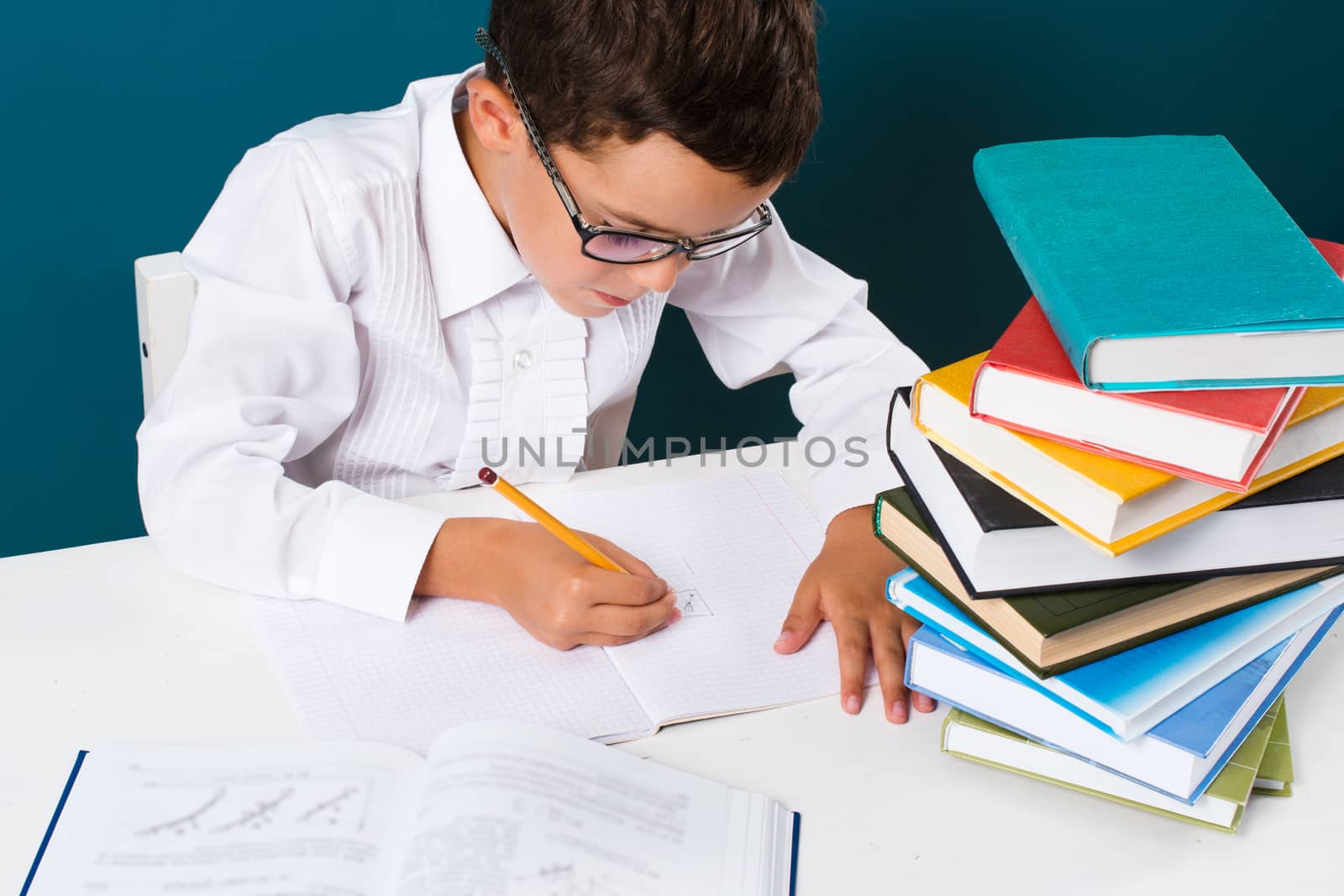 Pensive cute boy with homework sitting at a table, blue background