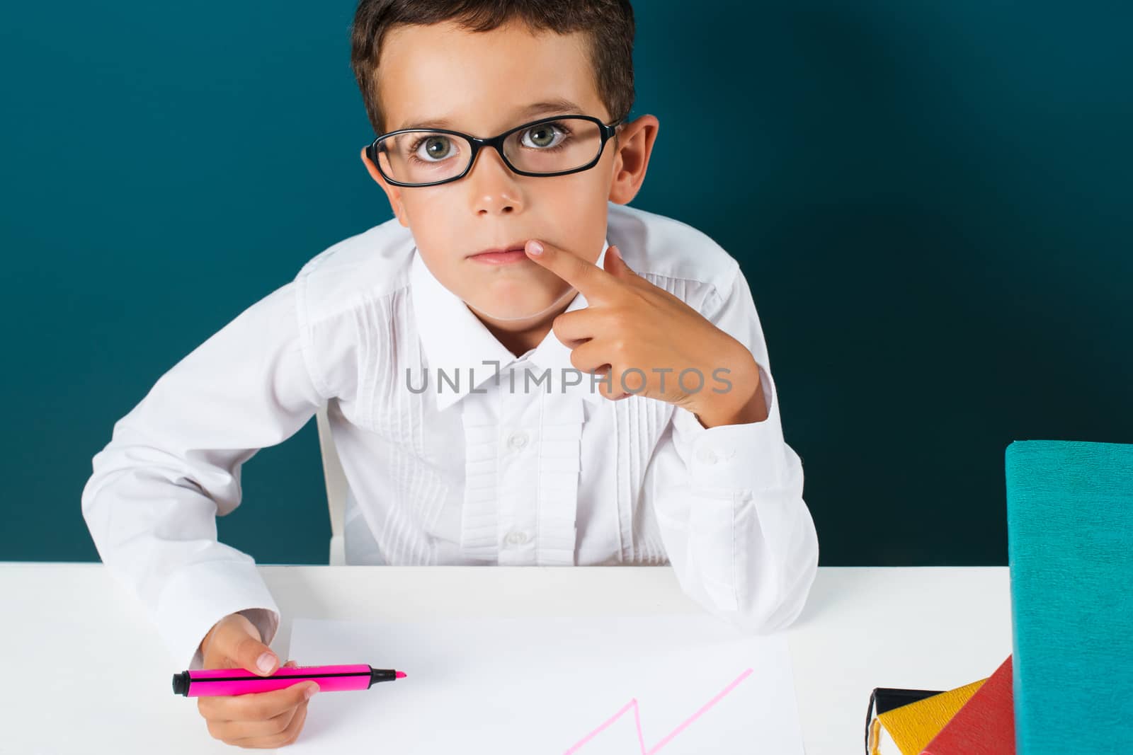 Pensive cute boy with glasses sitting at a table