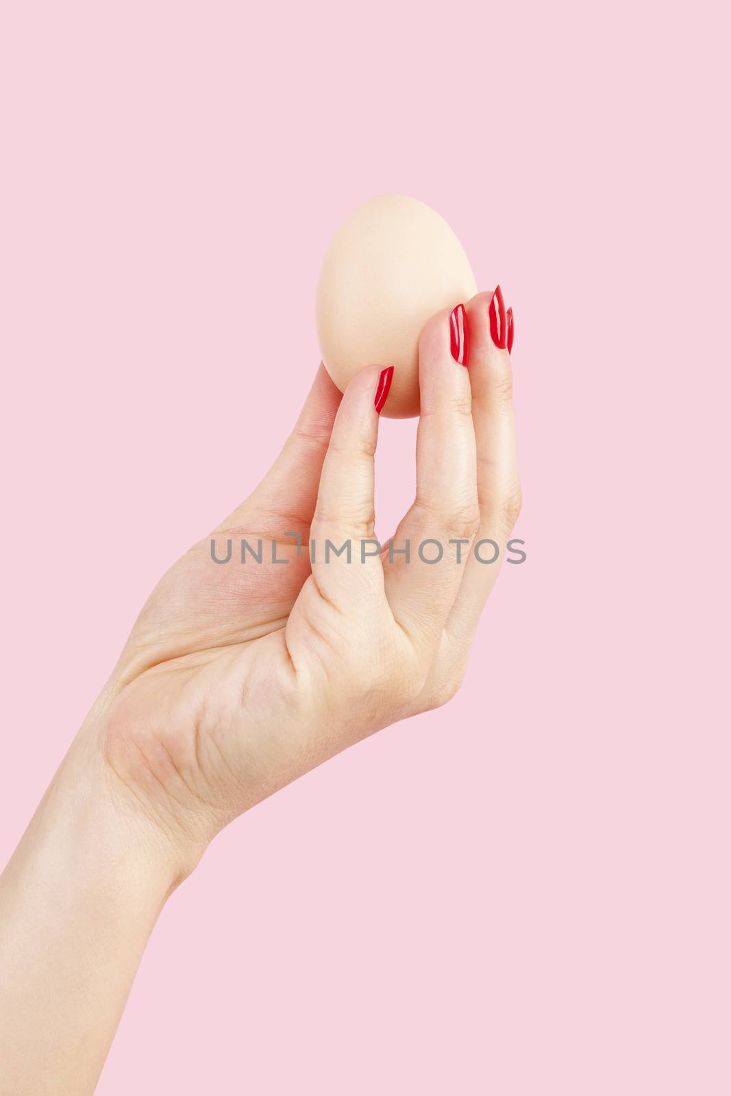 Female hand with red fingernails holding two eggs isolated on pink background. Feminism, emancipation, provocation and relationship problems.