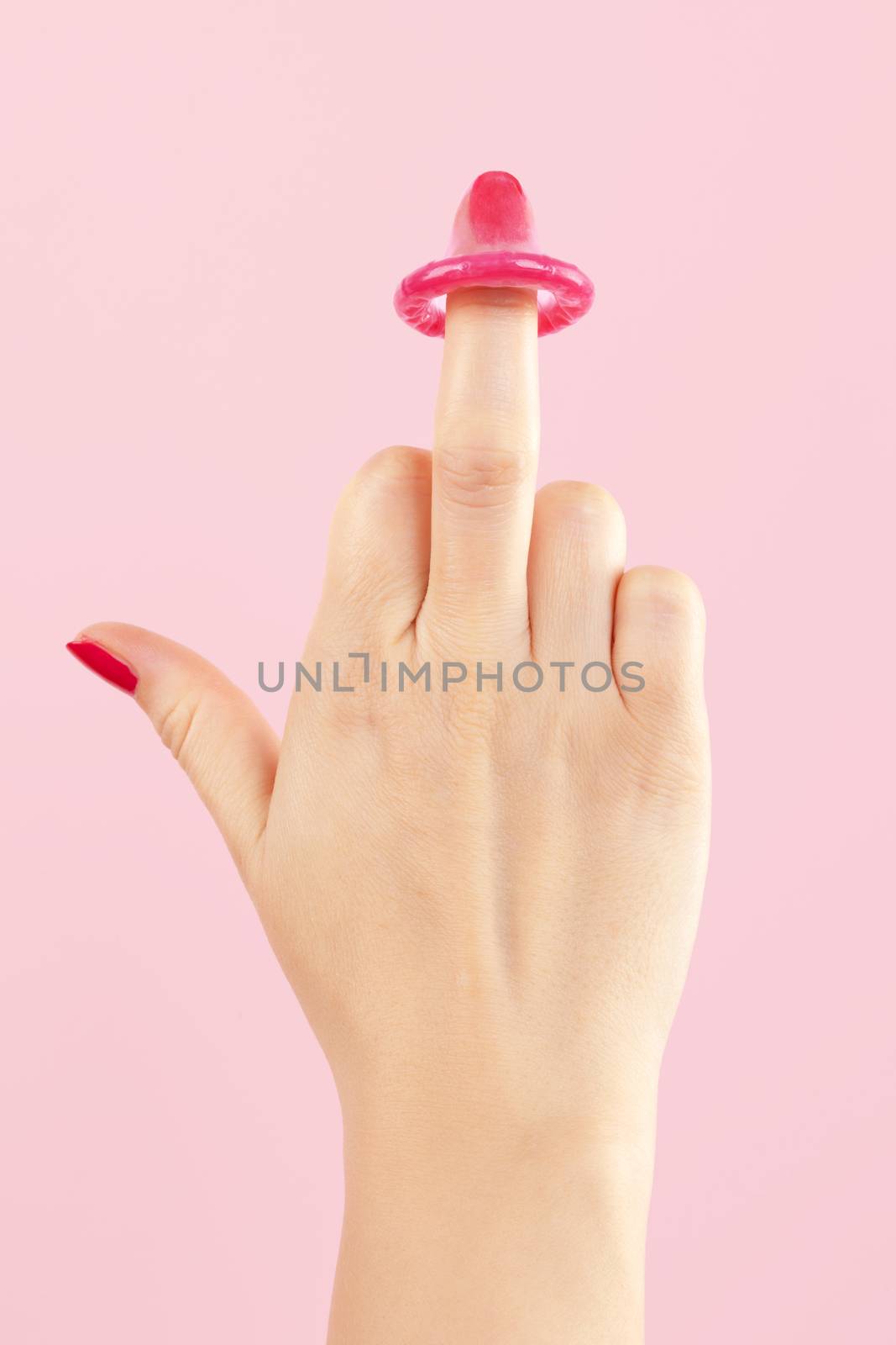 Female hand with red nails holding pink condom isolated on pink background. Safe sex and birth control concept. 
