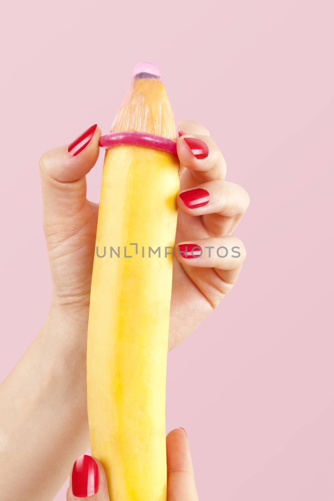 Female hand with red fingernails puts on a condom onto a banana. Safe sex concept.