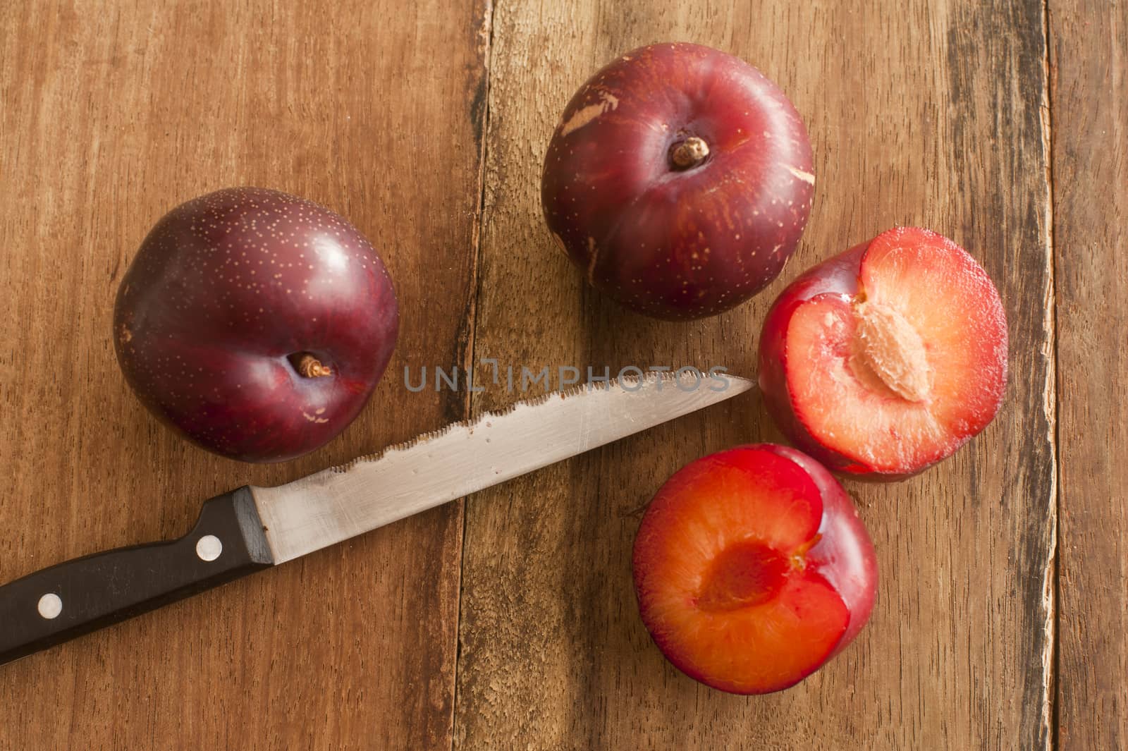 Organic Plums and Sharp Knife on Wooden Table by stockarch