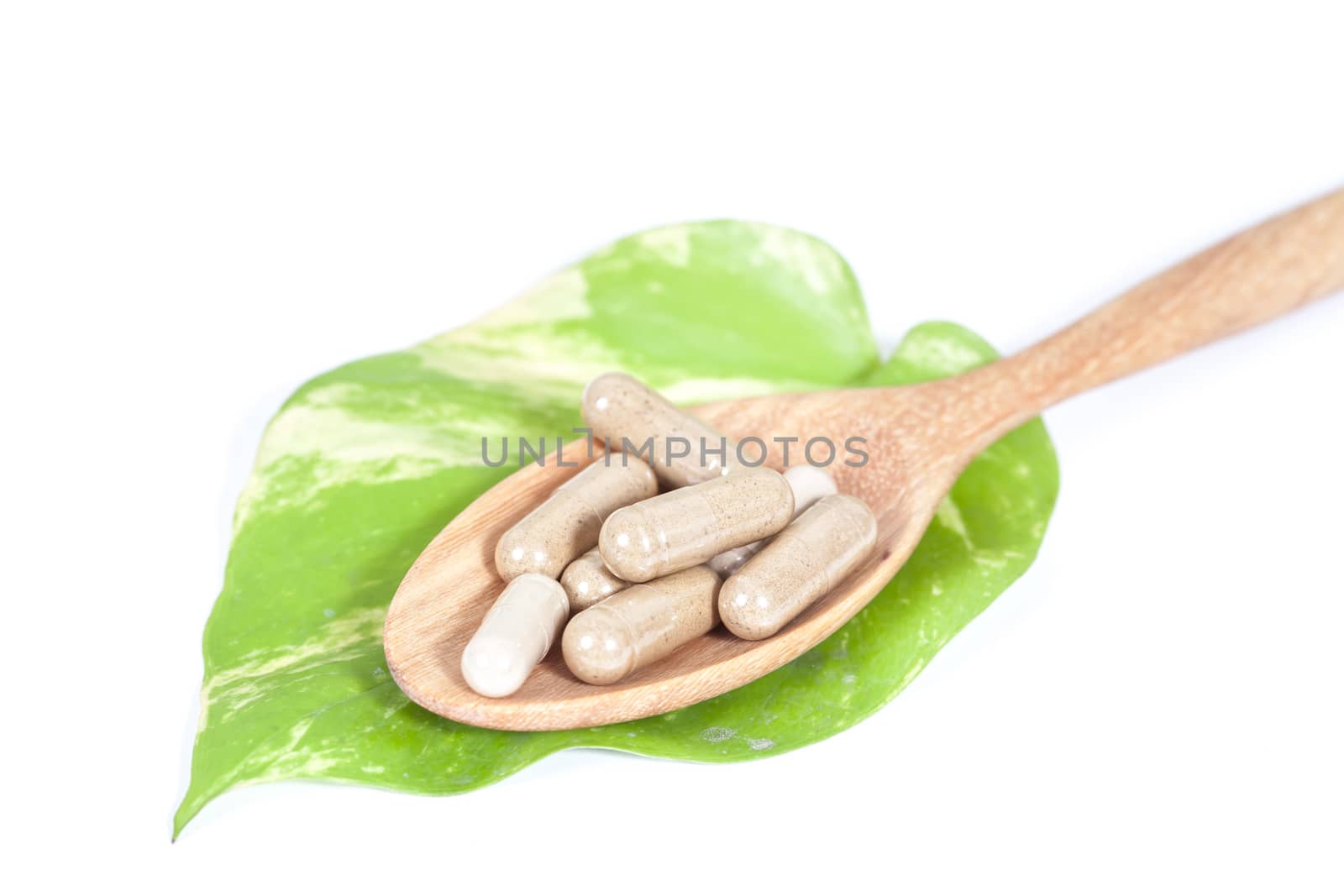 Capsules of herbs on spoon on white background 
