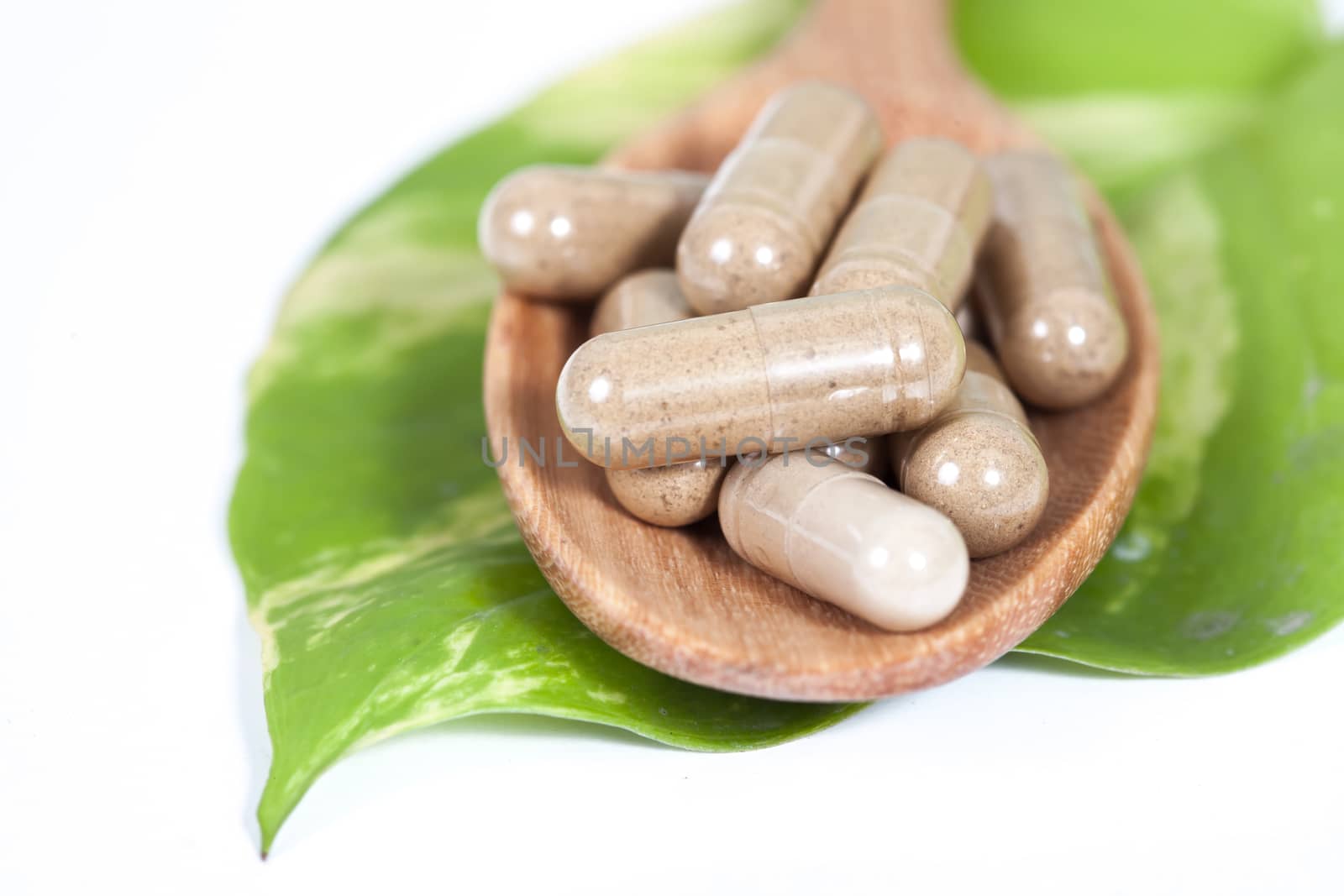 Capsules of herbs on spoon on white background 