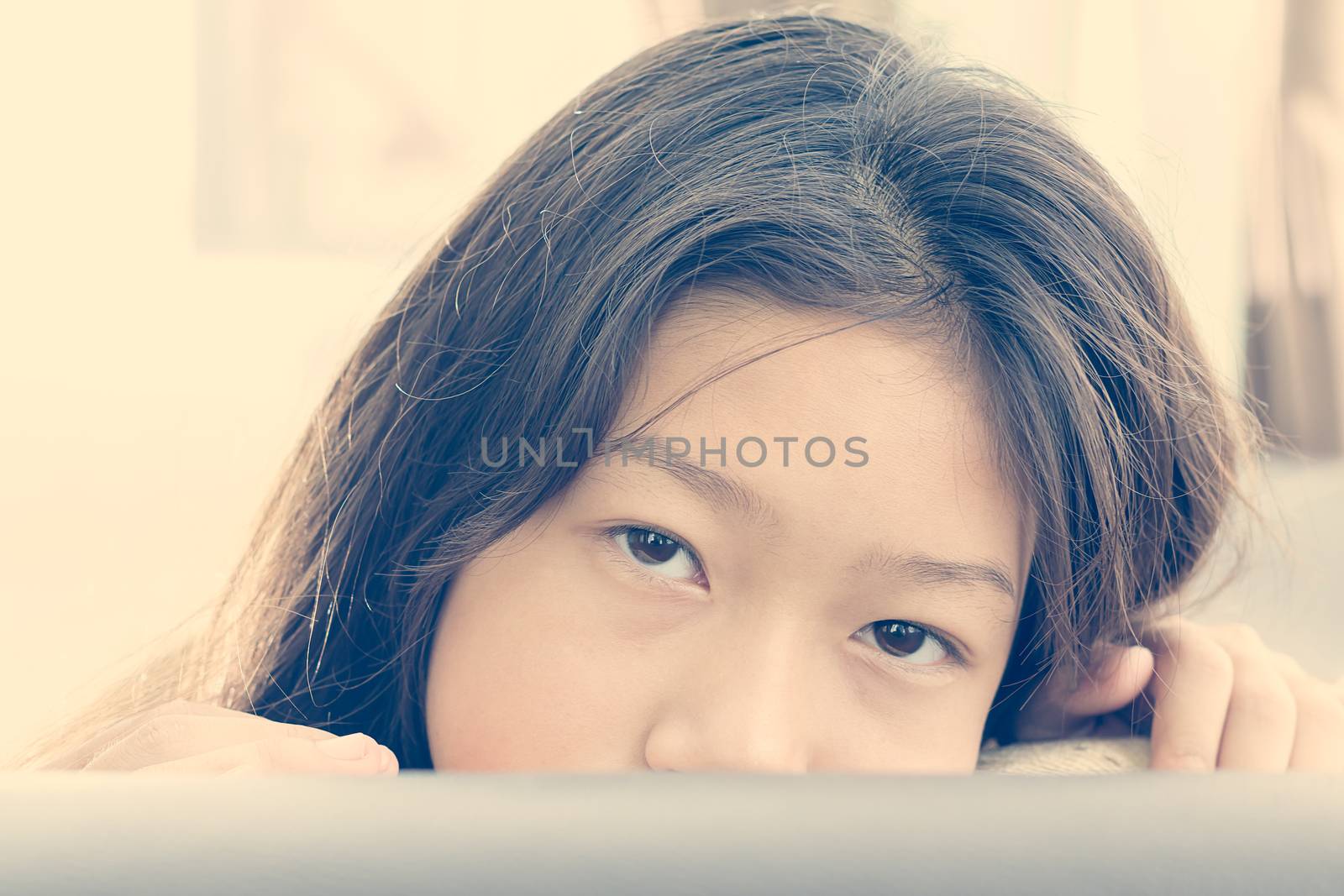 Cute asian girl peeking from of pillows on sofa