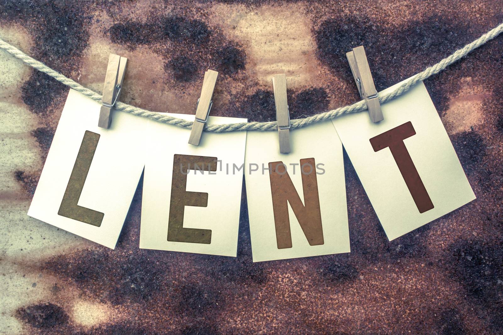 The word "LENT" stamped on cards and pinned to an old piece of twine over a rusted metal background.