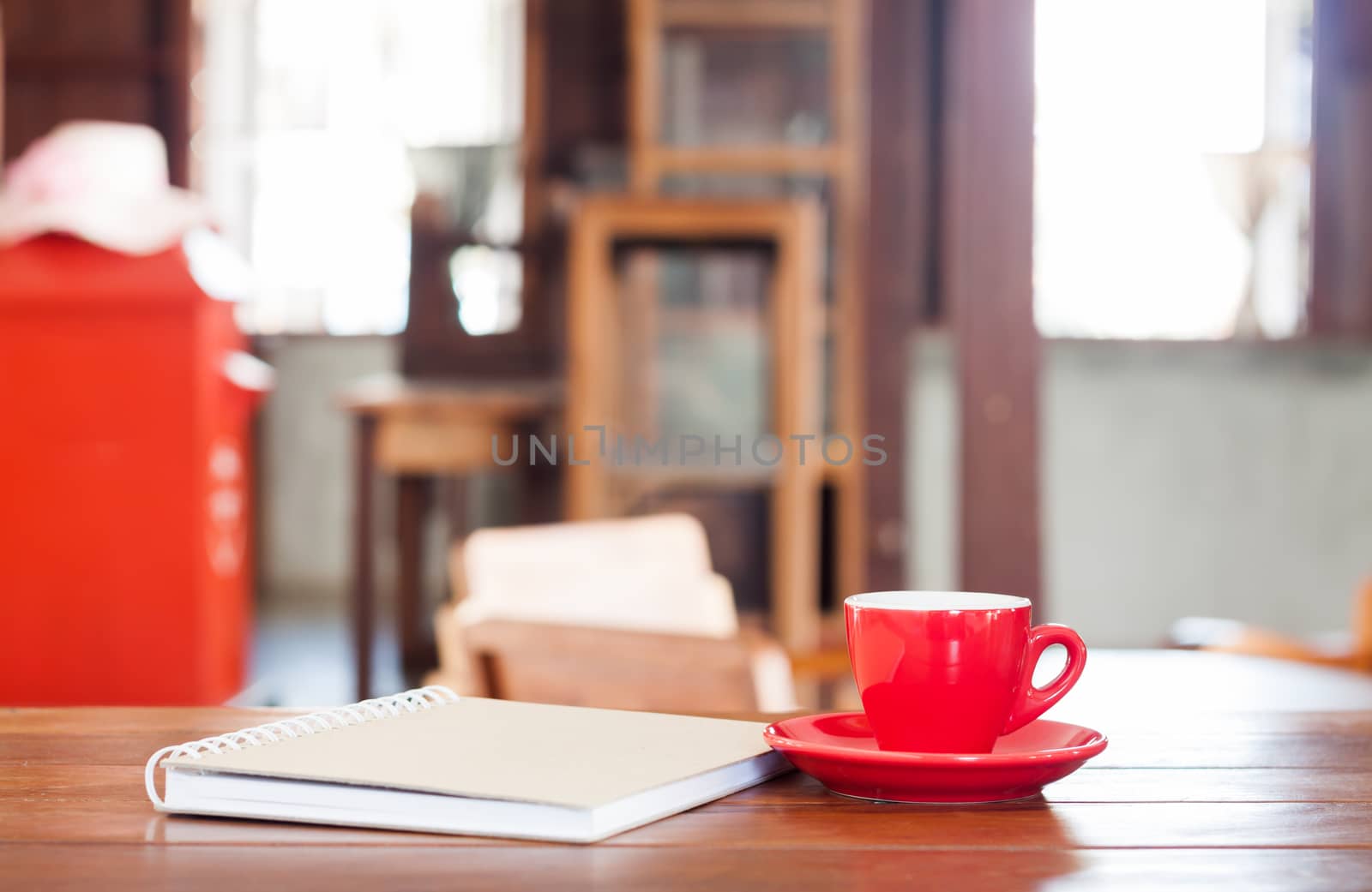 Red coffee cup with notebook on wooden table in coffee shop