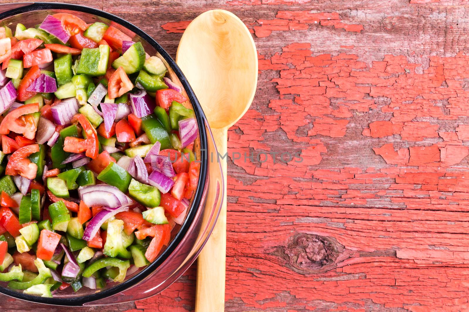 Bowl of healthy traditional Turkish shepherd salad with colorful finely diced assortment of fresh vegetables with a wooden serving spoon on an old grungy red picnic table with copy space