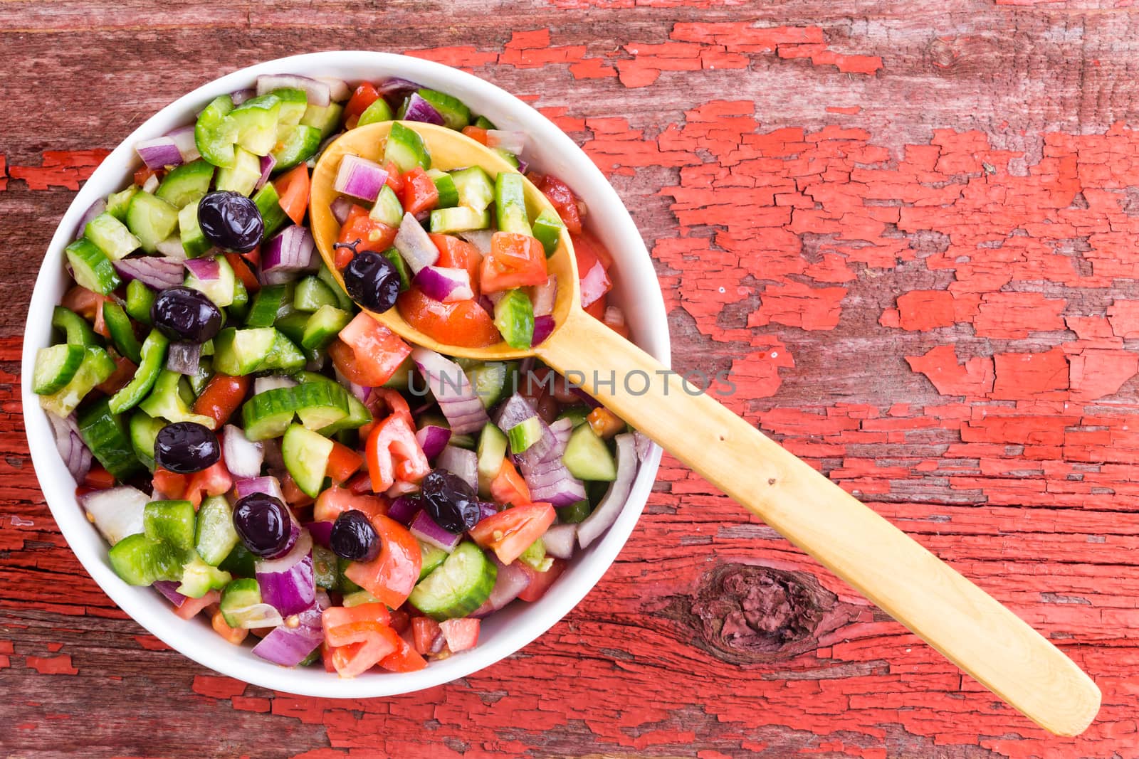 Healthy fresh Turkish shepherd salad made from a colorful assortment of diced fresh vegetables ready to be served in a round bowl on an old picnic table with grungy peeling red paint with copy space