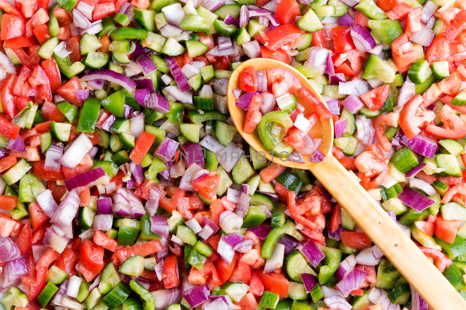 Colorful Turkish shepherd salad background food texture made from a variety of fresh finely diced vegetables with a wooden serving spoon viewed close up full frame from above