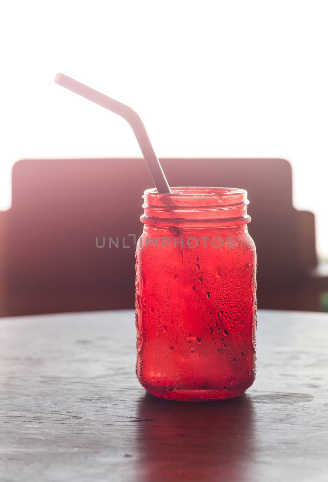 Iced drink in red glass on wooden table with vintage filter, stock photo