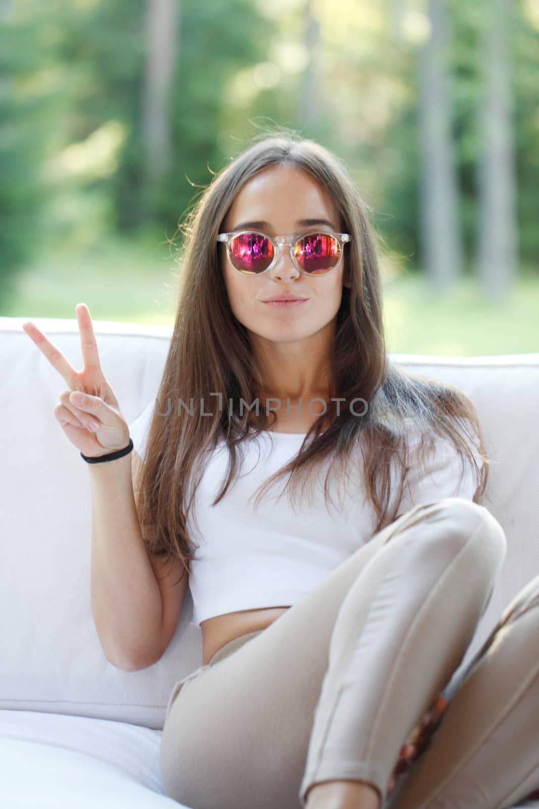 Young beautiful girl show victory sign sitting outdoors