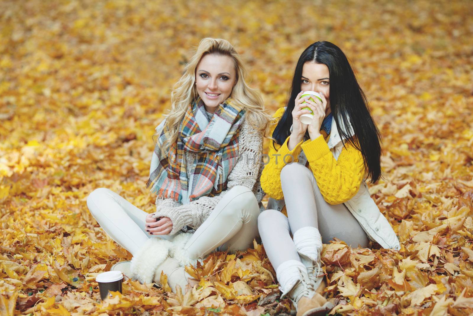 Two cheerful female friends drinking coffee in autumn park