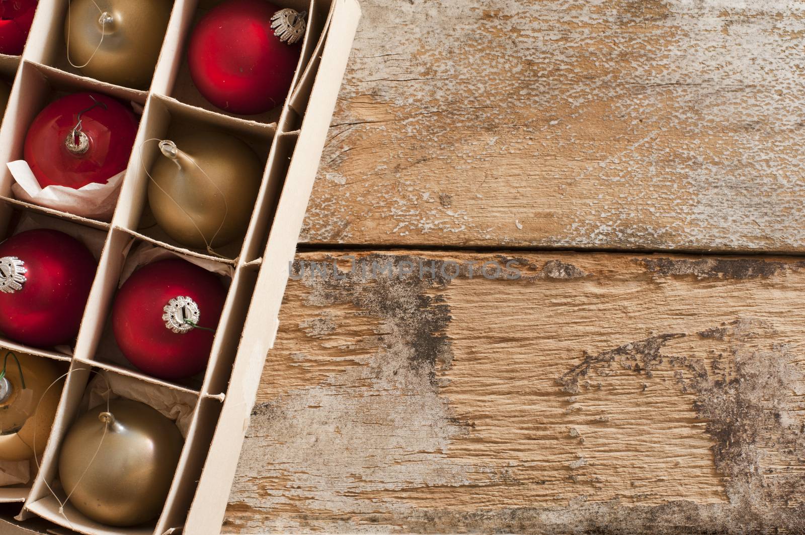 Box of packaged gold and red Christmas ornaments in neat compartments viewed from above on an old rustic wooden table with copy space for your seasonal greeting