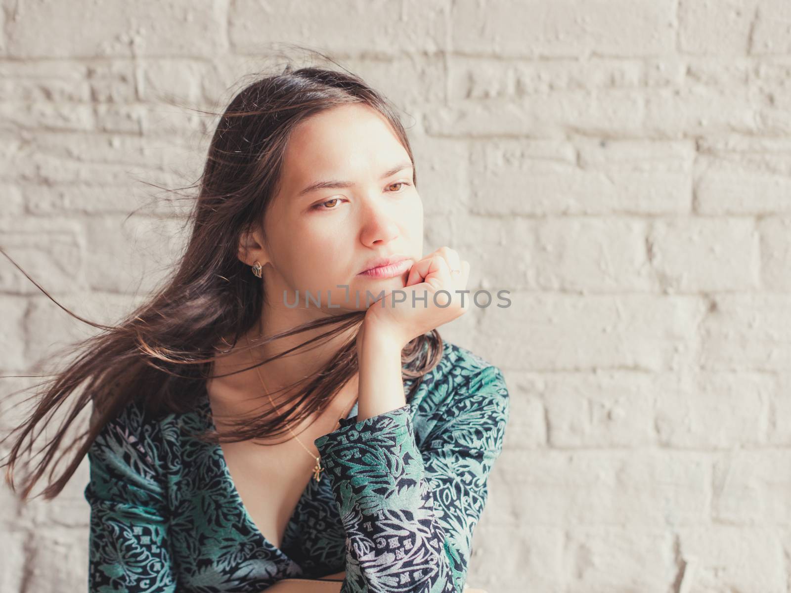 Stern and serious looking away young brunette beauty. Closeup portrait of serious young woman with sensual look away. Girl rests her chin on hand and serious looking away. Copy space