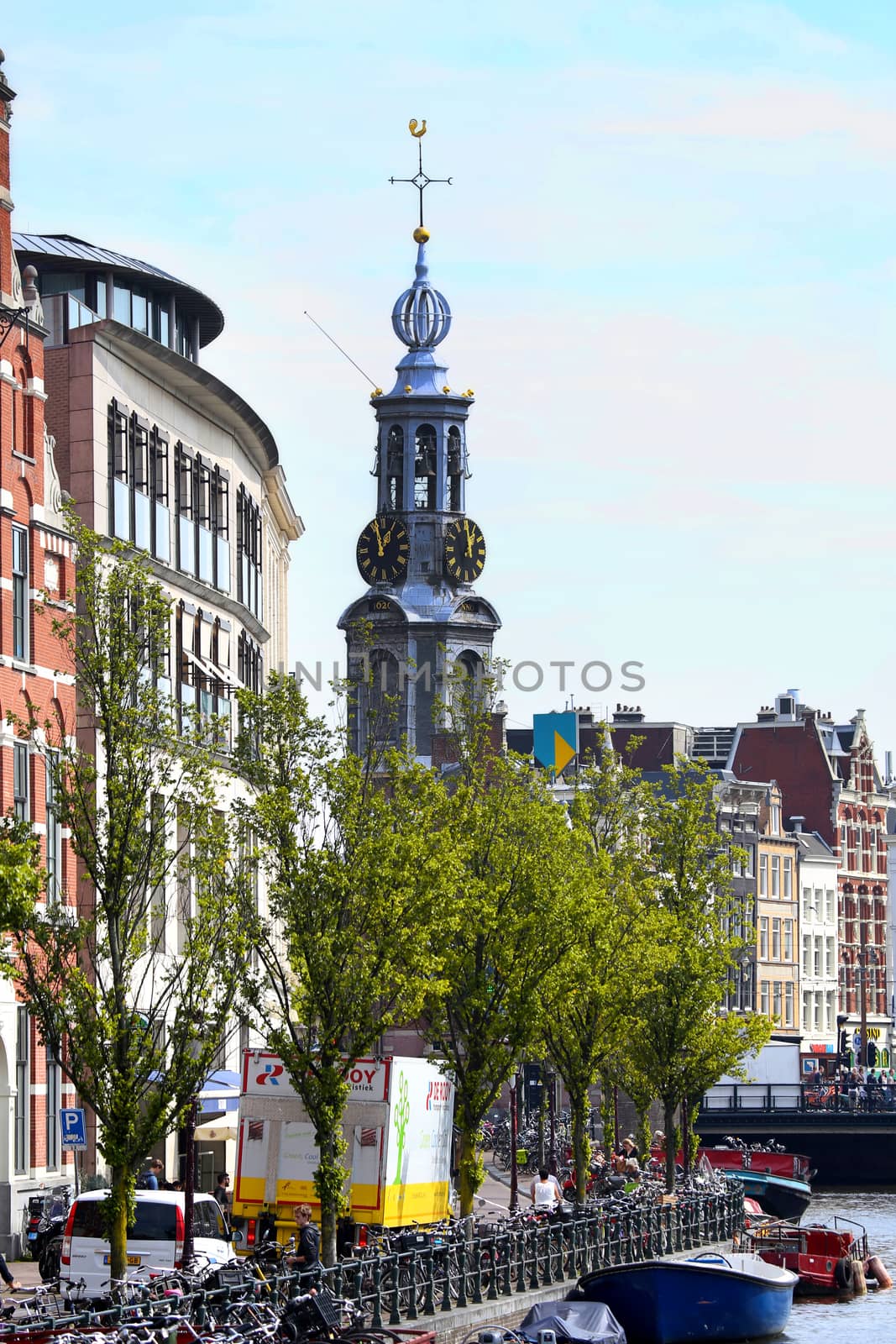 AMSTERDAM, THE NETHERLANDS - AUGUST 19, 2015: View on Bloemenmarkt and The Munttoren ("Coin Tower") from Koningsplein. People walk on the street Singel. Street life, Canal, bicycle and boat in Amsterdam. Amsterdam is capital of the Netherlands on August 19, 2015.