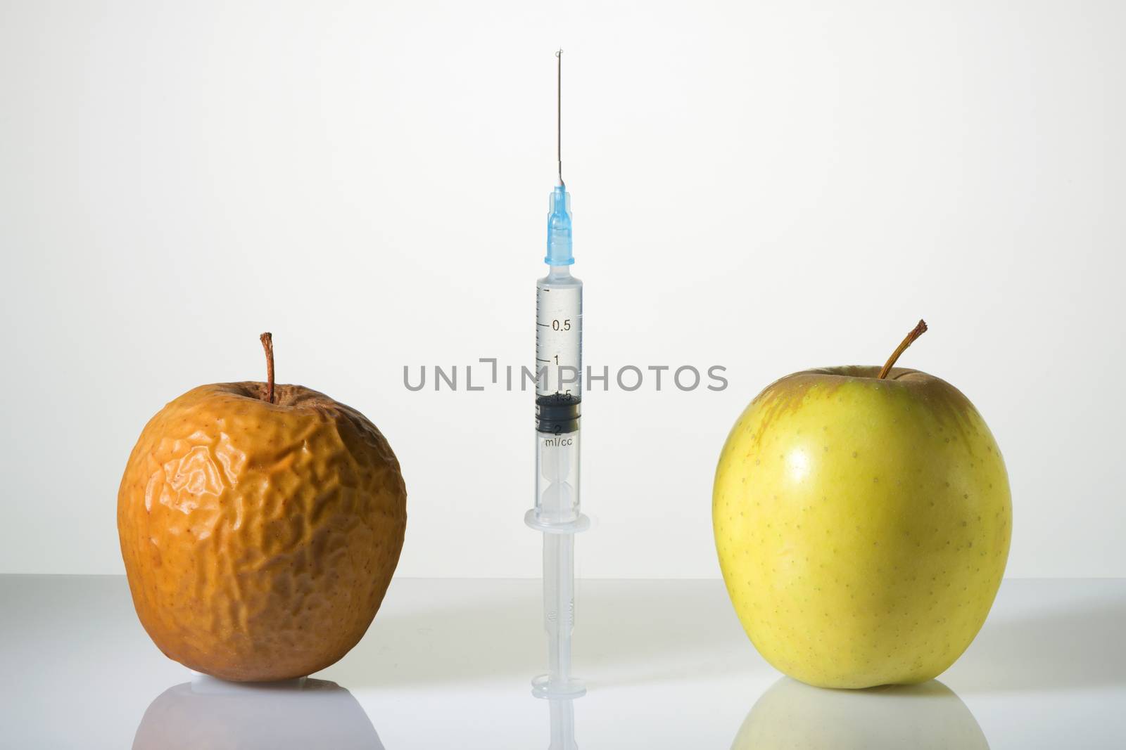 Wrinkled and smooth apples and the syringe between them